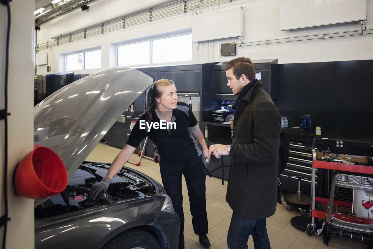 Customer discussing with female mechanic while standing by car at auto repair shop