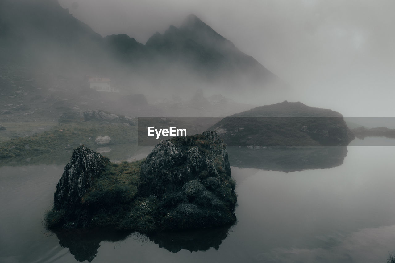 Scenic view of lake by rock formation amidst fog