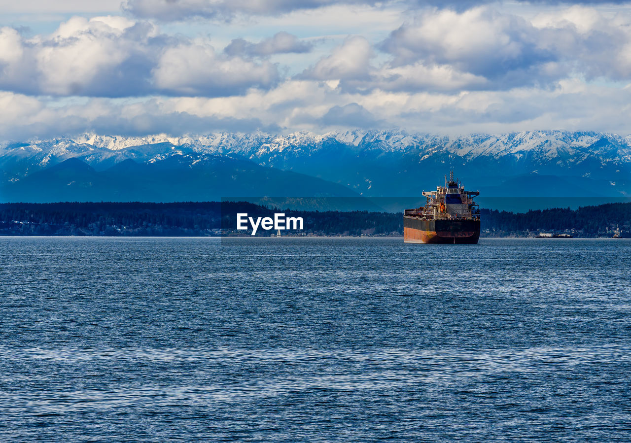 A tanker ship in elliott bay with the olympic mouintain range in the distance.