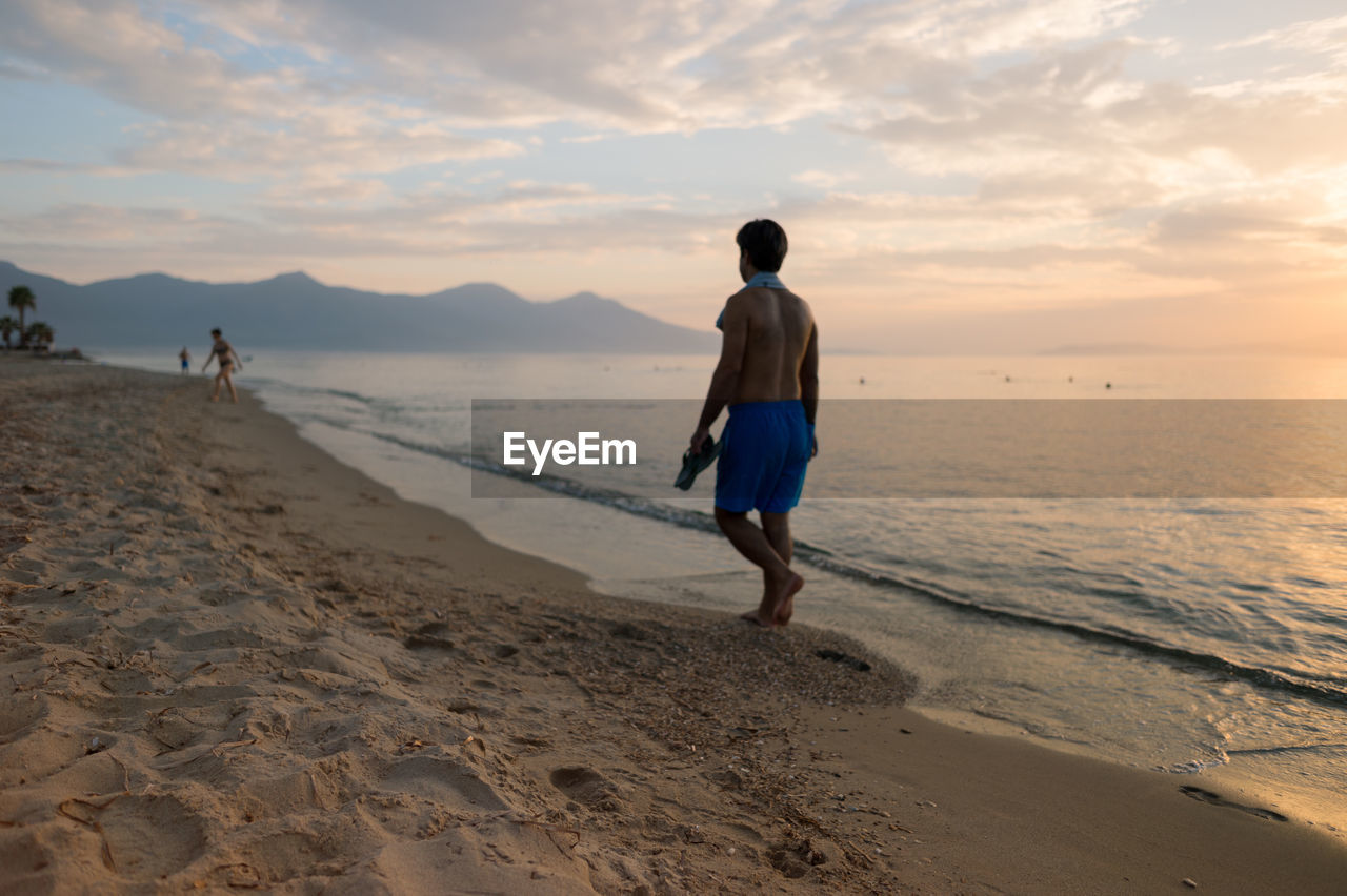 Rear view full length of man walking on shore at beach during sunset