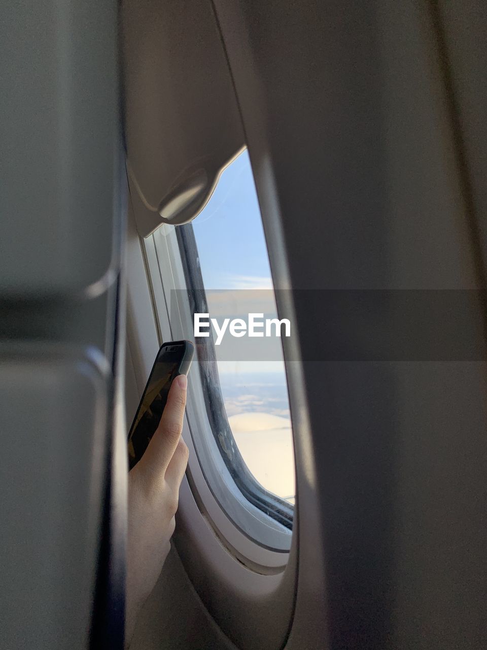 Cropped hand of woman using smart phone by window in airplane
