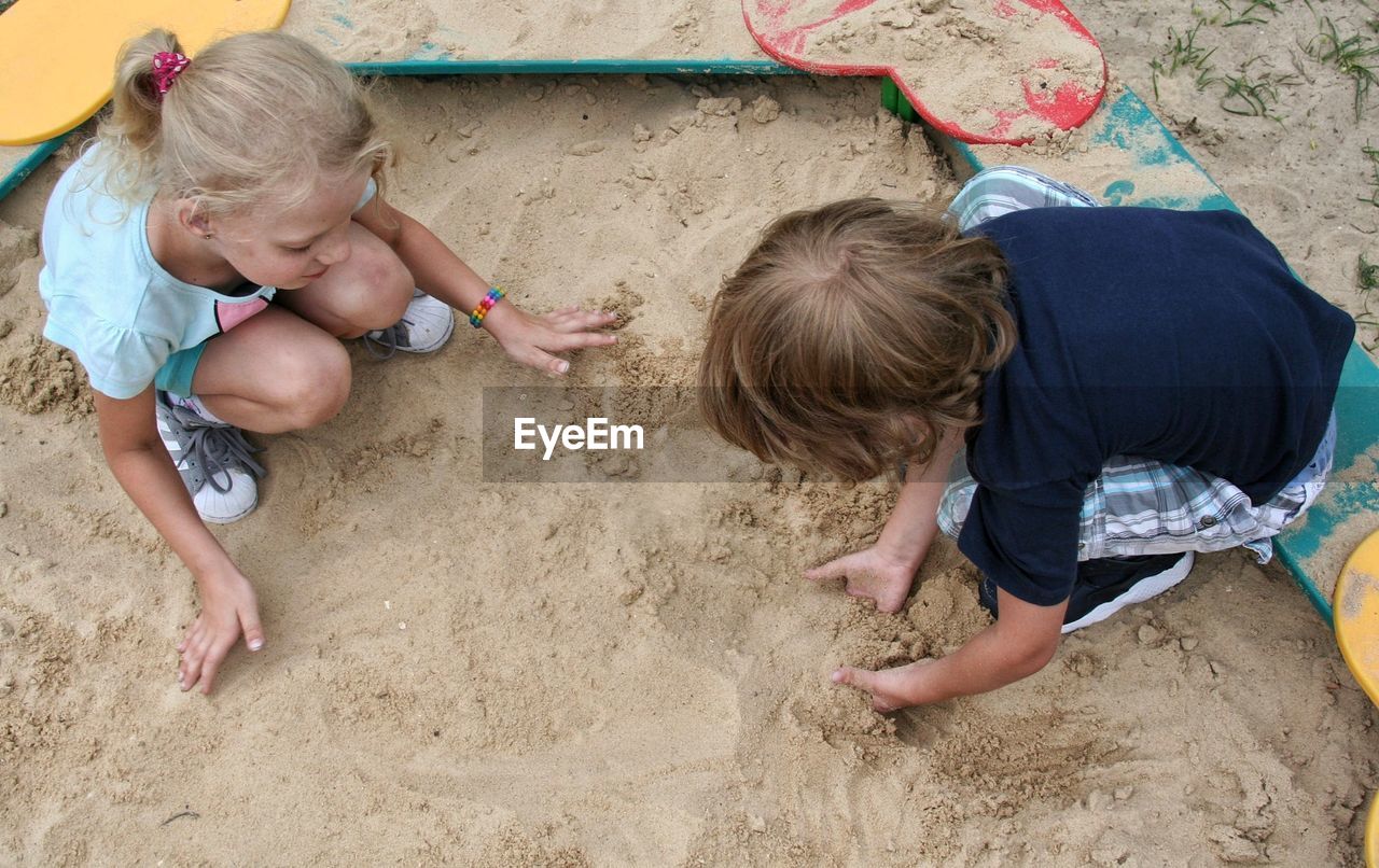 High angle view of siblings playing with sand on shore at beach