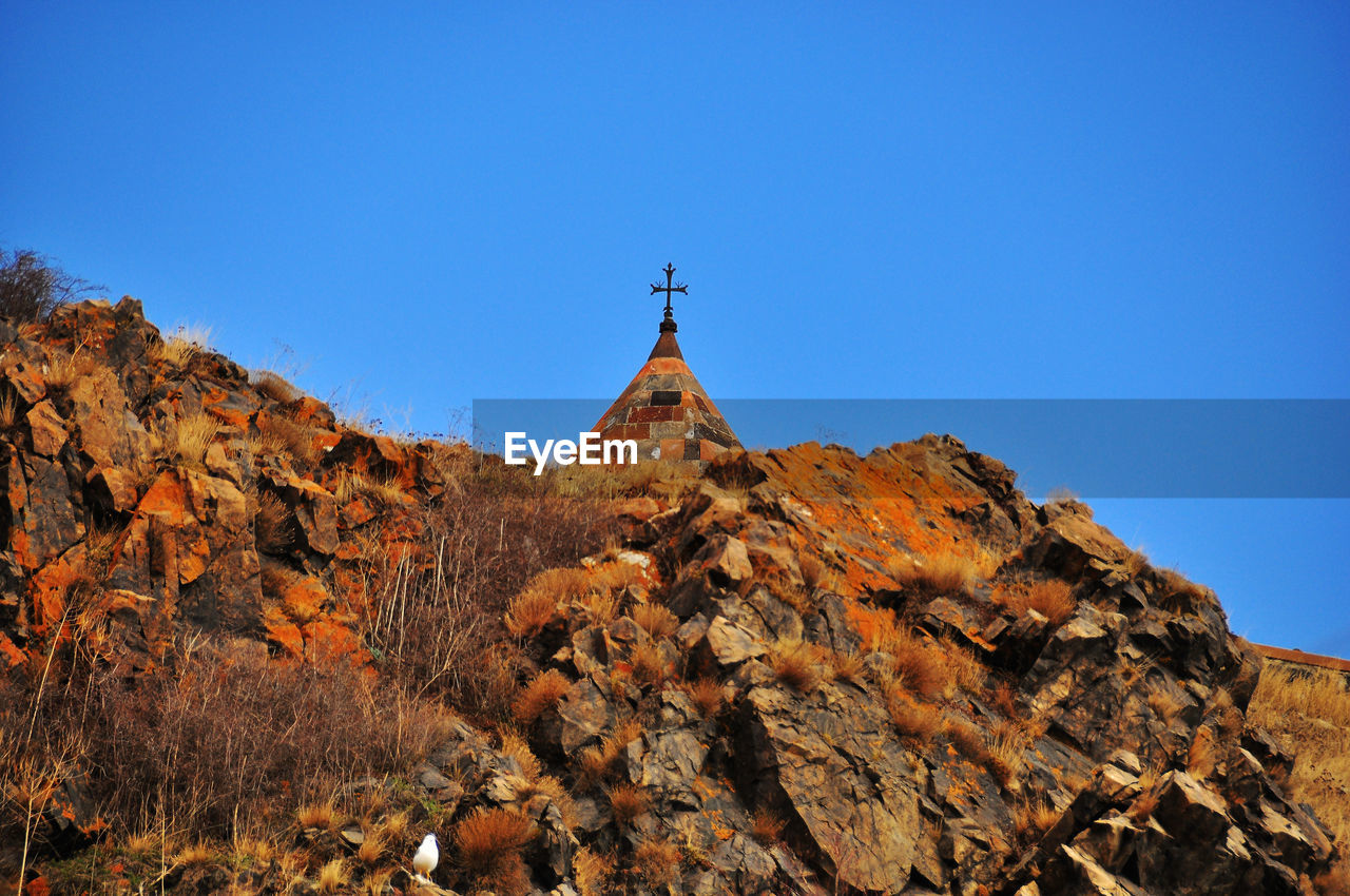 Low angle view of cross on rock against sky