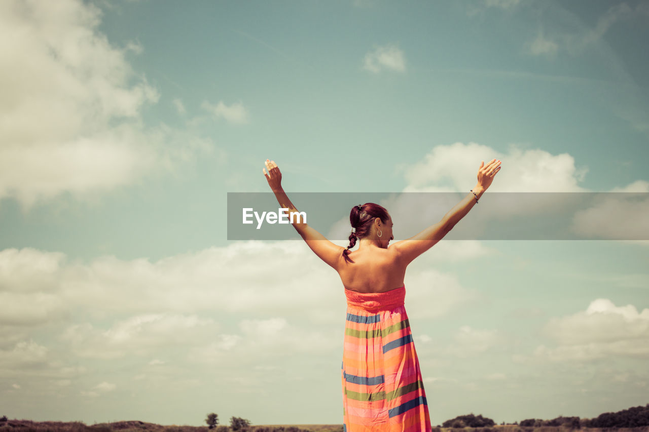 Rear view of carefree woman with arms outstretched against the sky. copy space.