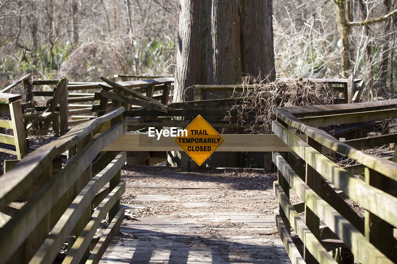 sign, communication, transport, bridge, track, tree, text, warning sign, wood, no people, nature, day, plant, western script, forest, outdoors, information sign, railing, architecture, sunlight, road sign, urban area, road, land