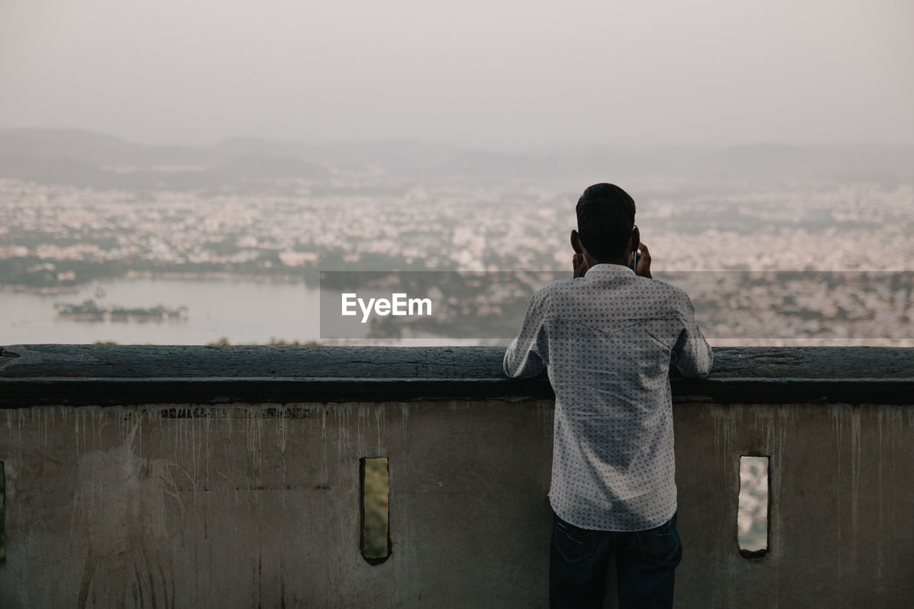 Rear view of man looking at a city against sky