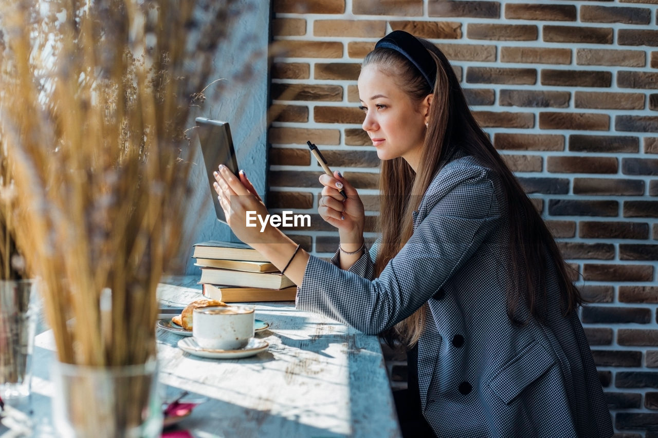 A beautiful young woman uses a tablet for video communication at a table in a cafe. 