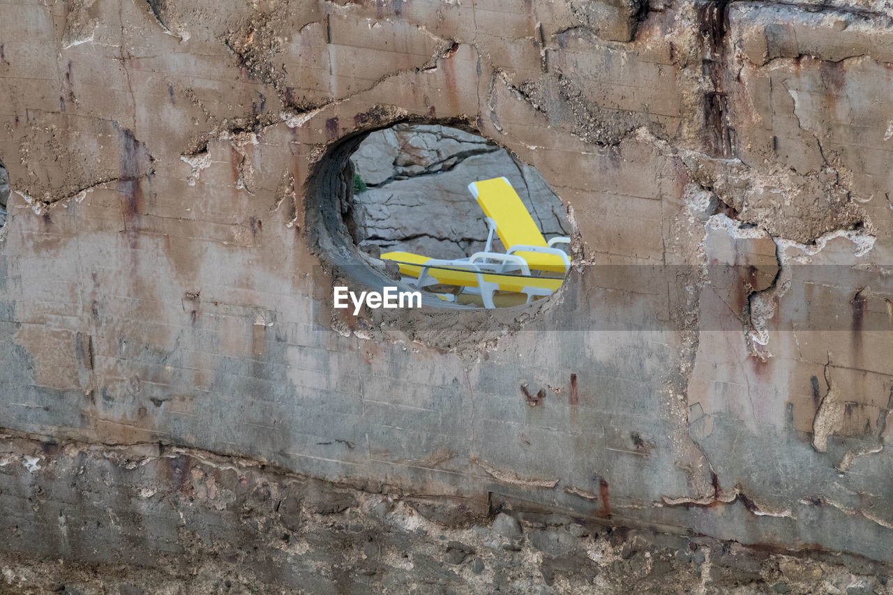 Yellow lounge chairs seen through hole in old wall