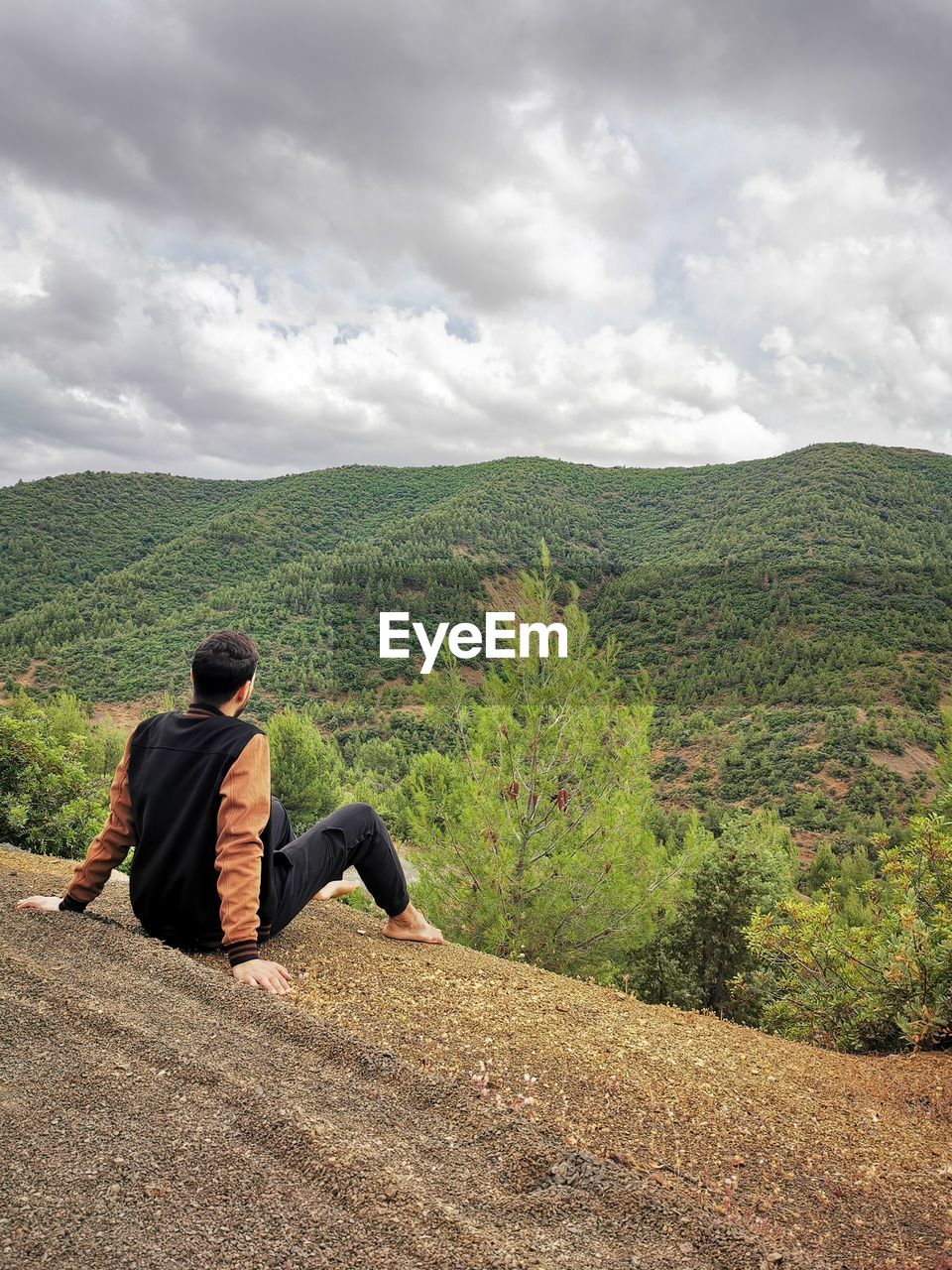 Rear view of man sitting on mountain against sky