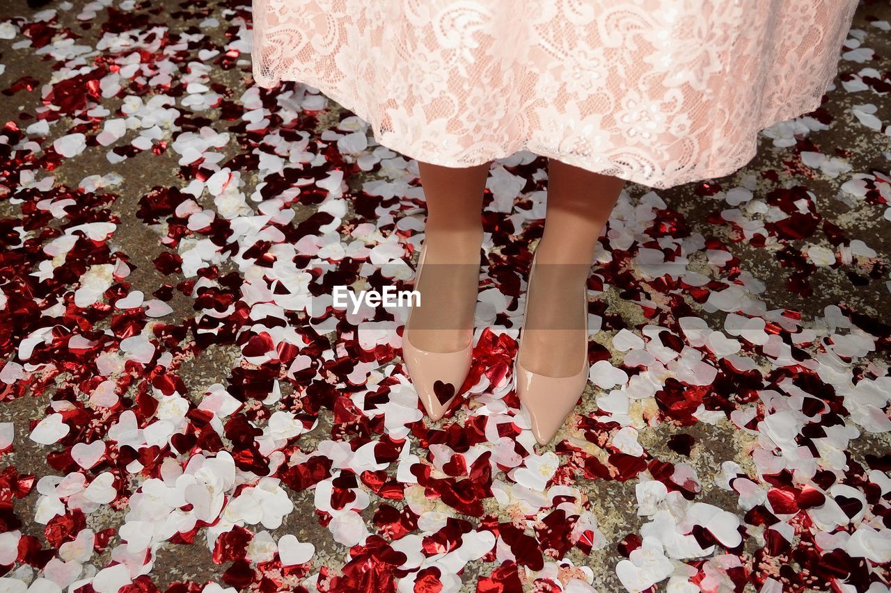 Detail of wedding dress with pink shoes, surrounded by heart-shaped confetti

