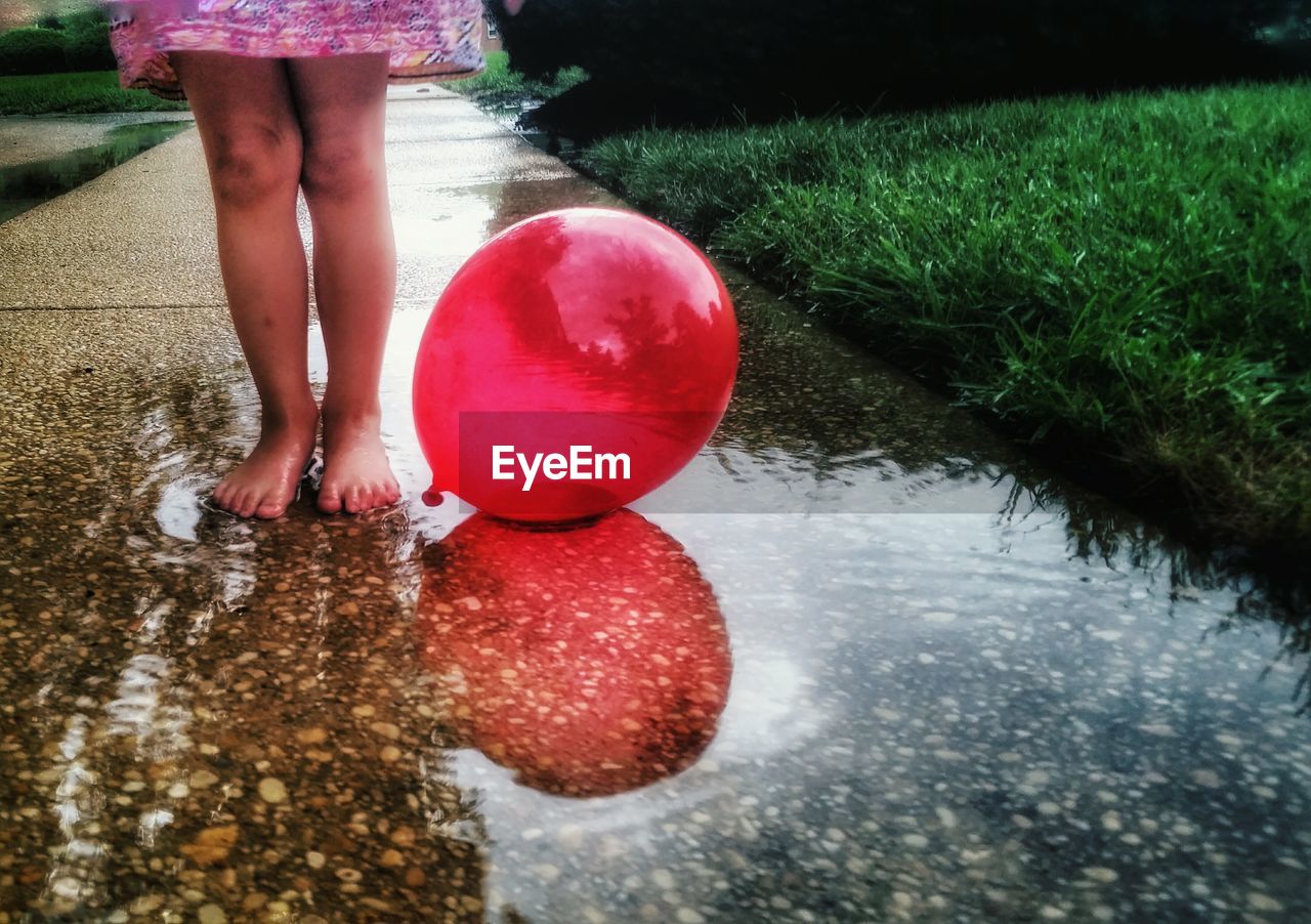 Low section of girl standing by balloon in puddle on footpath