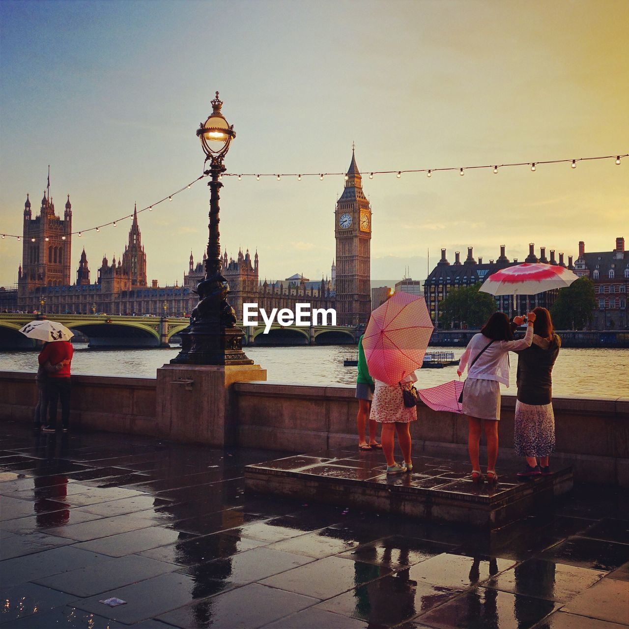 People standing by thames river looking at big ben in city during rainy season