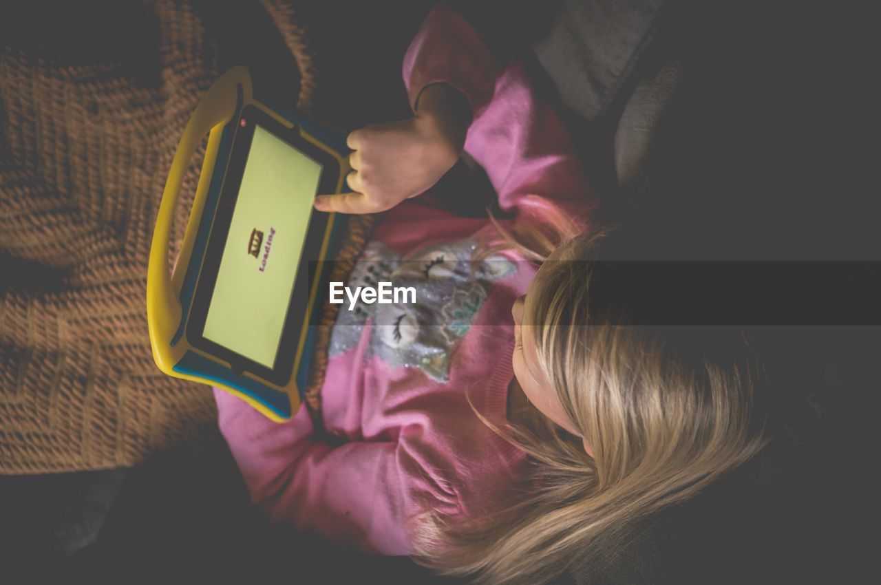 High angle view of girl using digital tablet while lying on bed at home