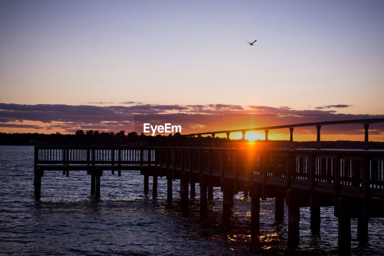 SILHOUETTE OF BIRDS FLYING OVER SEA AGAINST SKY DURING SUNSET