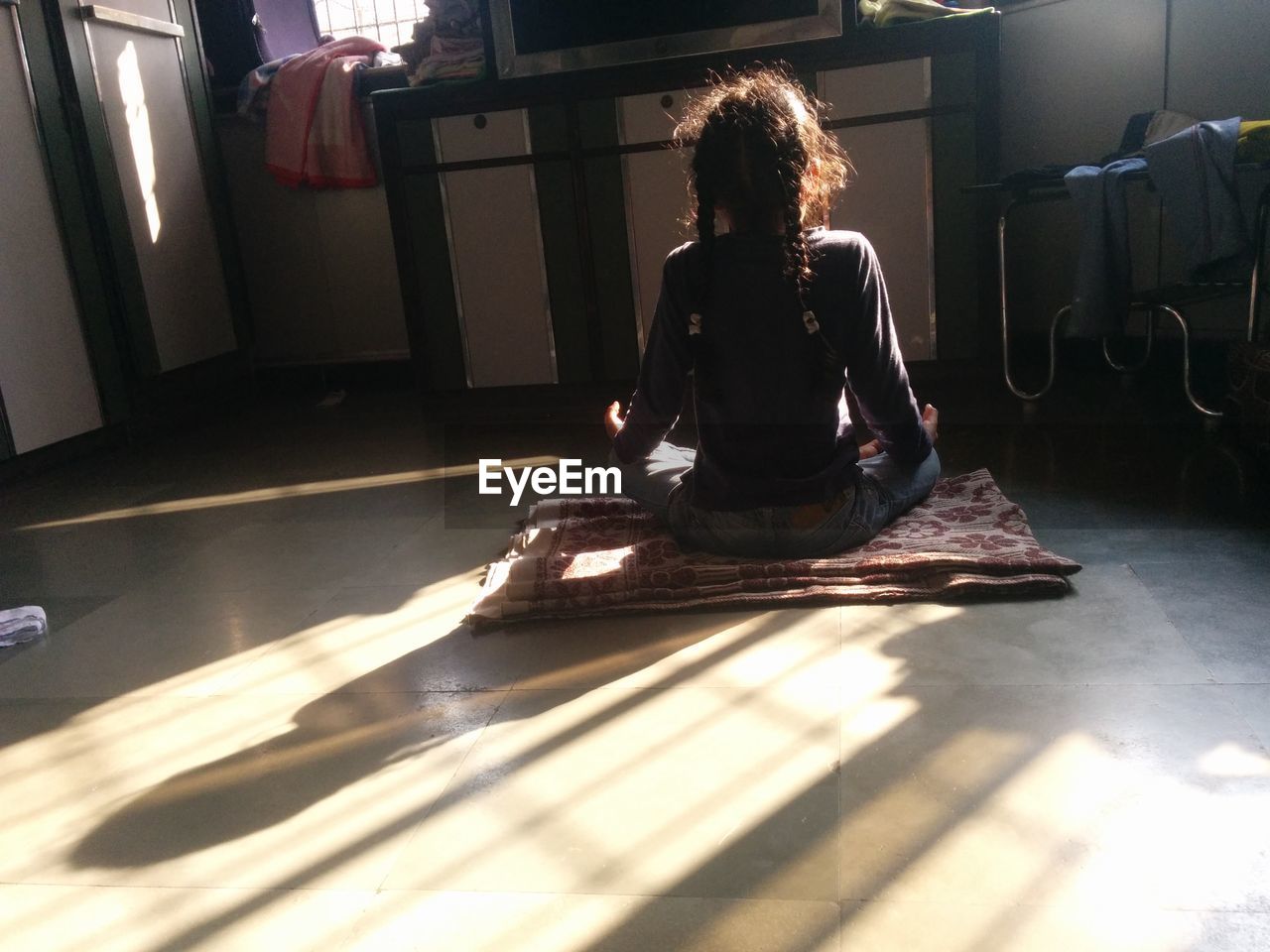 Rear view of girl doing yoga on floor at home