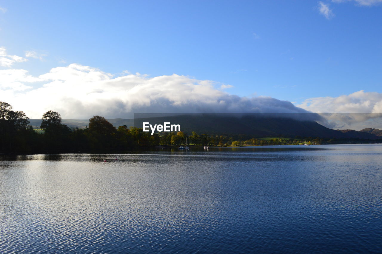 Scenic view of lake with clouds over mountains against sky