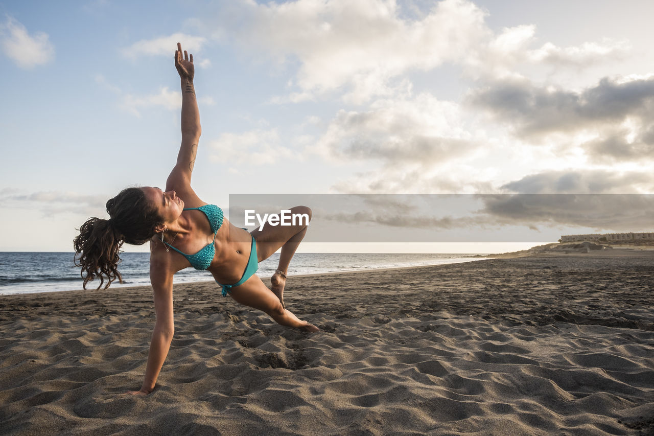 Woman in bikini practicing yoga at beach