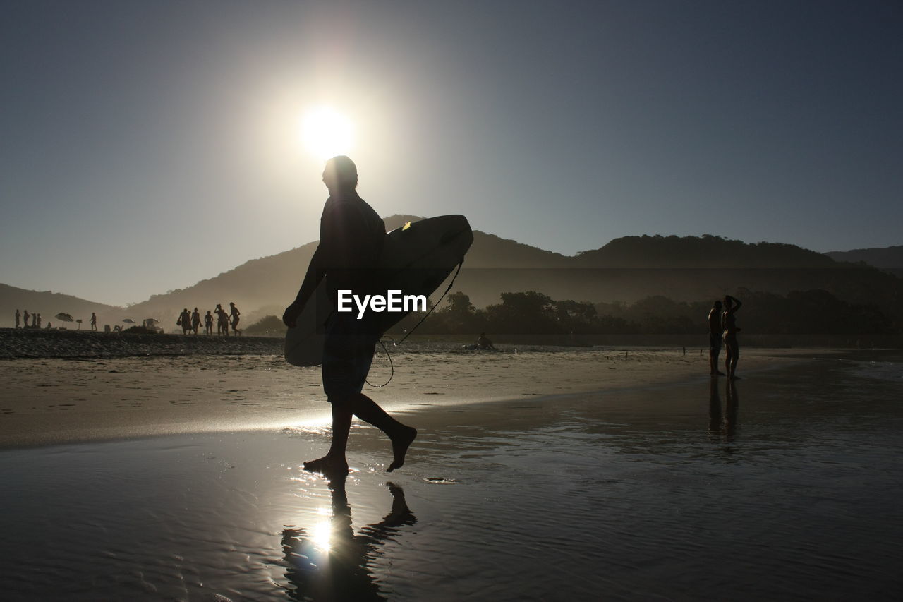 SILHOUETTE OF MEN ON BEACH AGAINST SKY