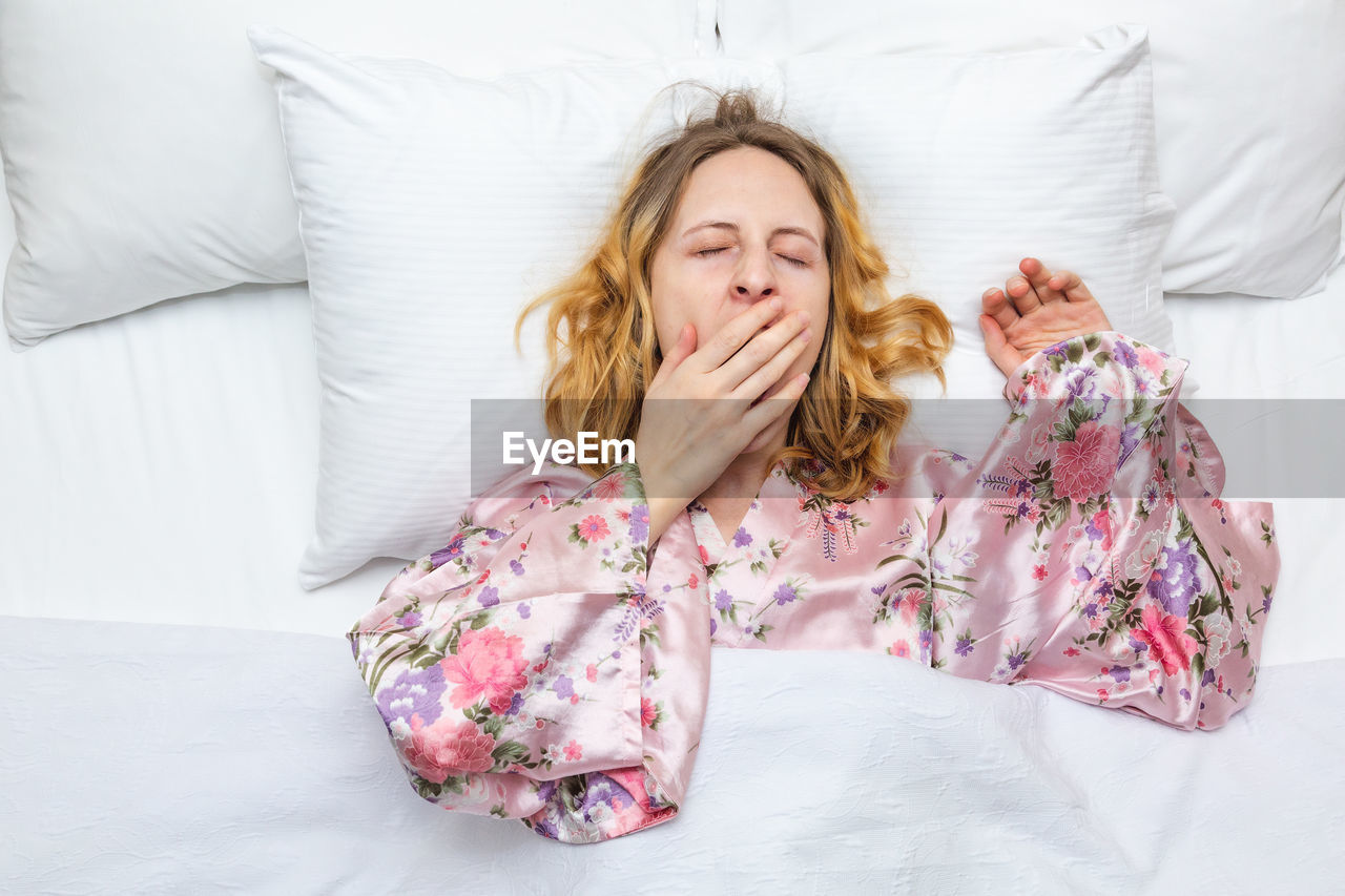 YOUNG WOMAN SITTING ON BED IN BEDROOM