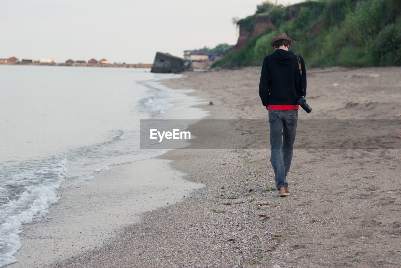 Rear view full length of man walking with camera at beach