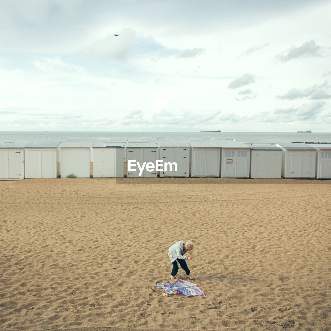 Rear view of child standing on beach against sky