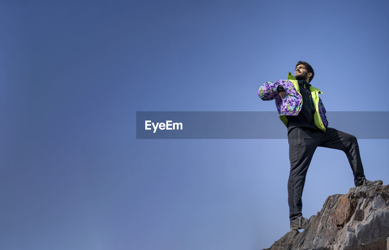 LOW ANGLE VIEW OF MAN STANDING ON ROCK