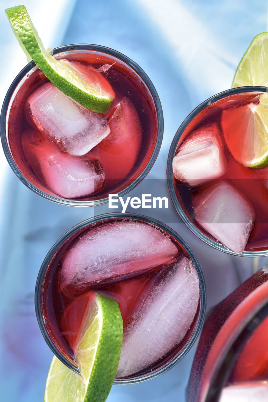 Above view of drink glasses of red hibiscus flower iced tea with ice cubes with lime slices garnish