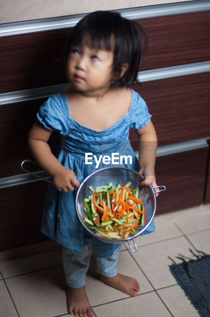 High angle view of girl holding container with carrot and zucchini in kitchen at home