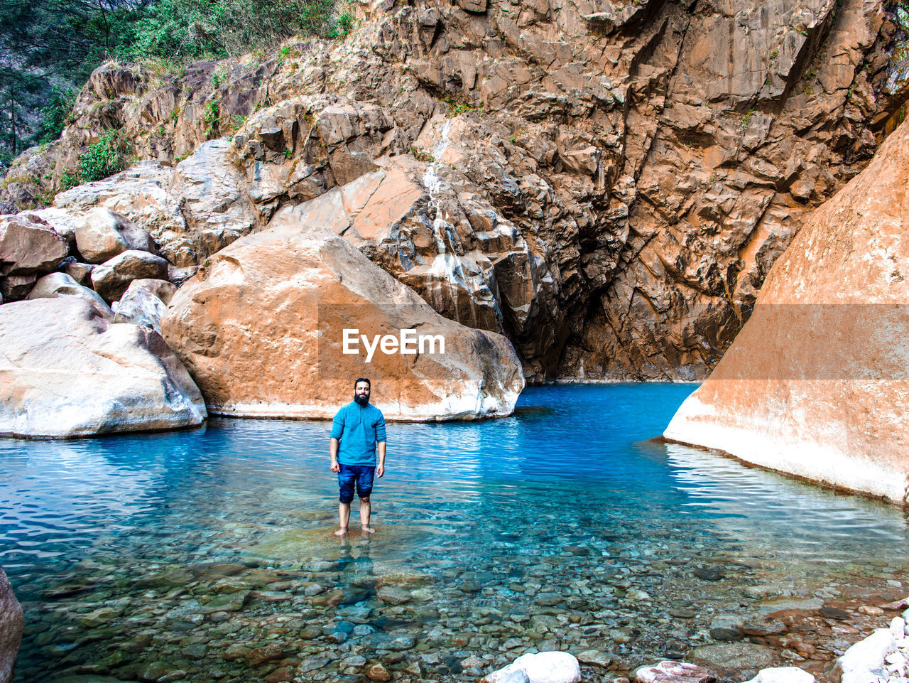 Rear view of man standing on rock by the base of waterfall