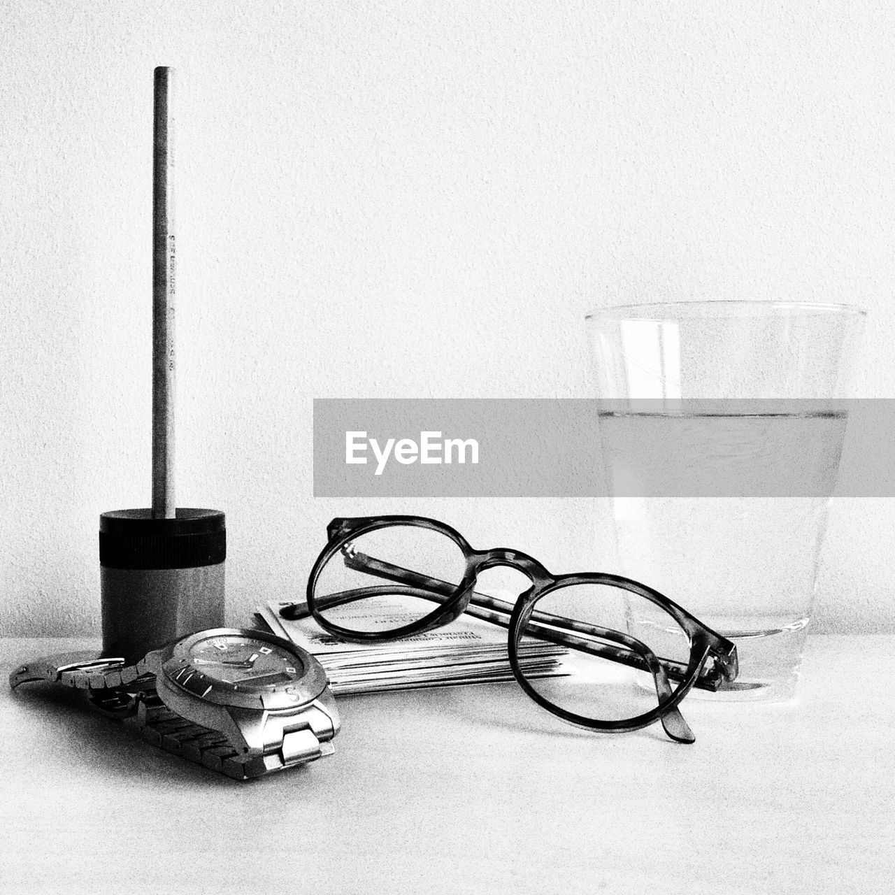 Eyeglasses by drinking glass and wrist watch on table in office