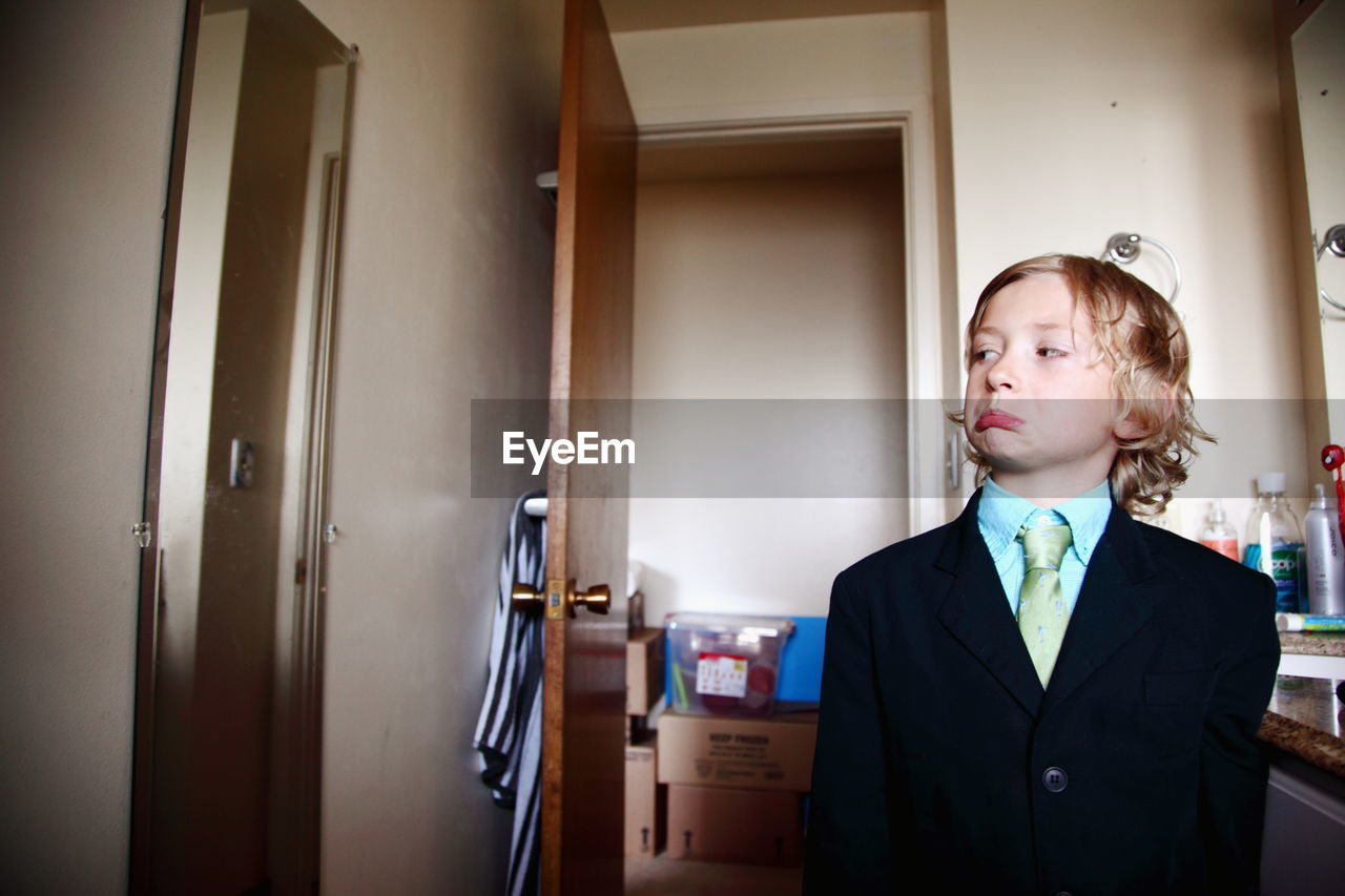 Boy in suit making face while standing in bathroom