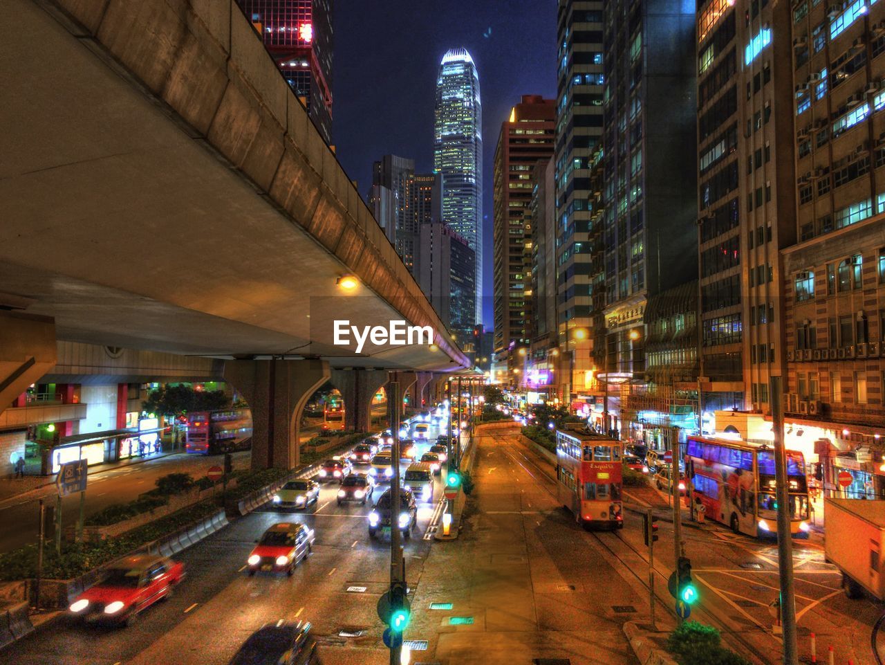 Illuminated vehicles on street amidst buildings and bridge in city