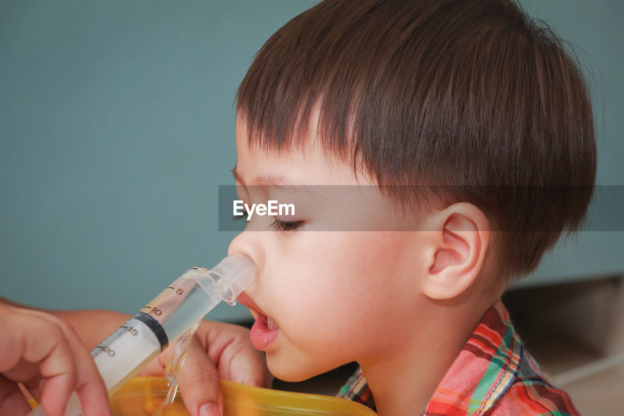 Cropped hand spraying water in boy nose