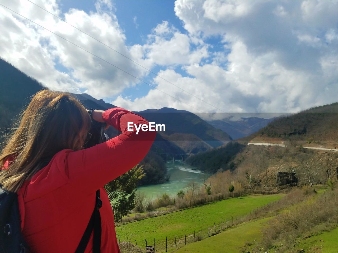 Rear view of woman photographing valley against cloudy sky