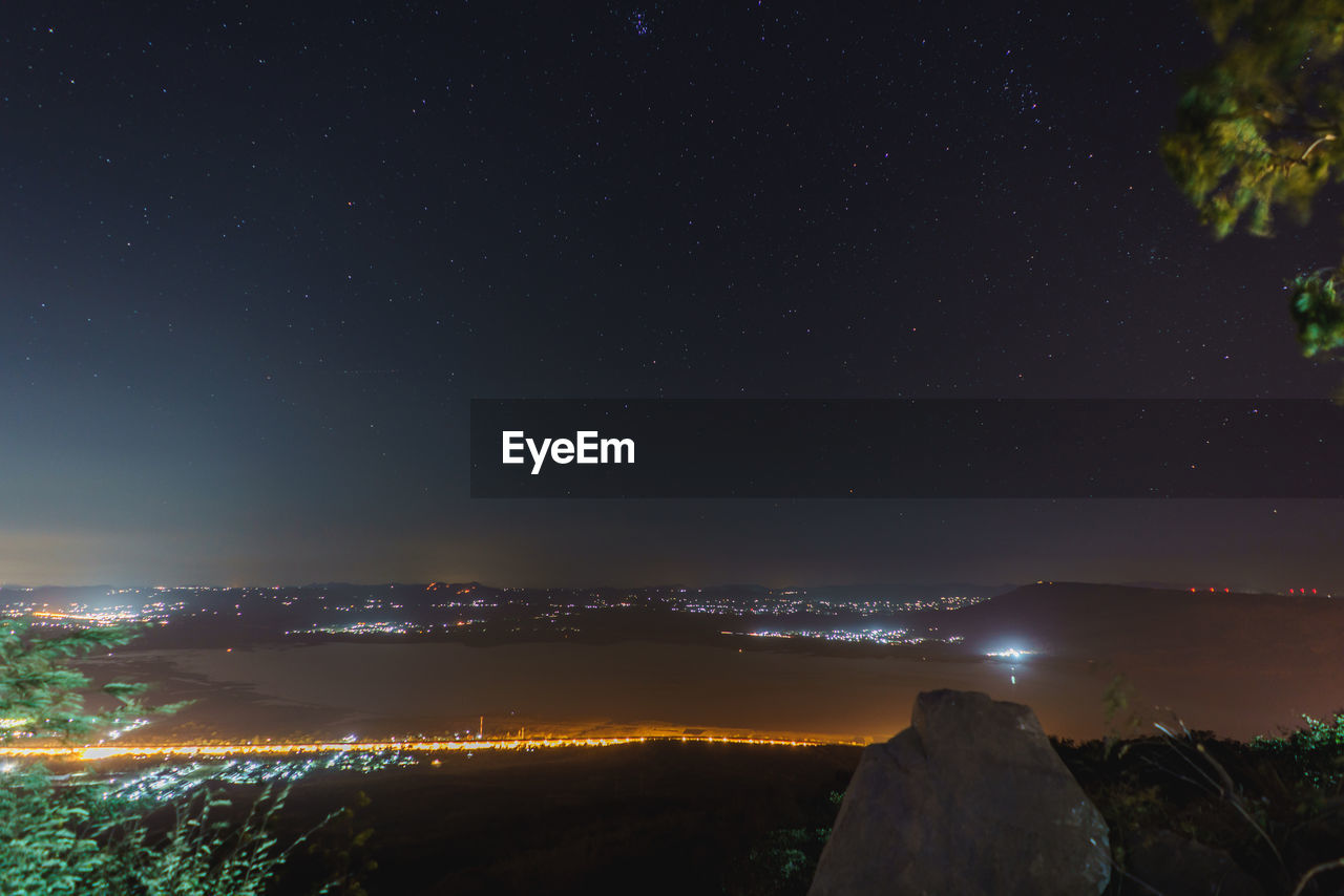 AERIAL VIEW OF ILLUMINATED CITYSCAPE AGAINST SKY AT NIGHT