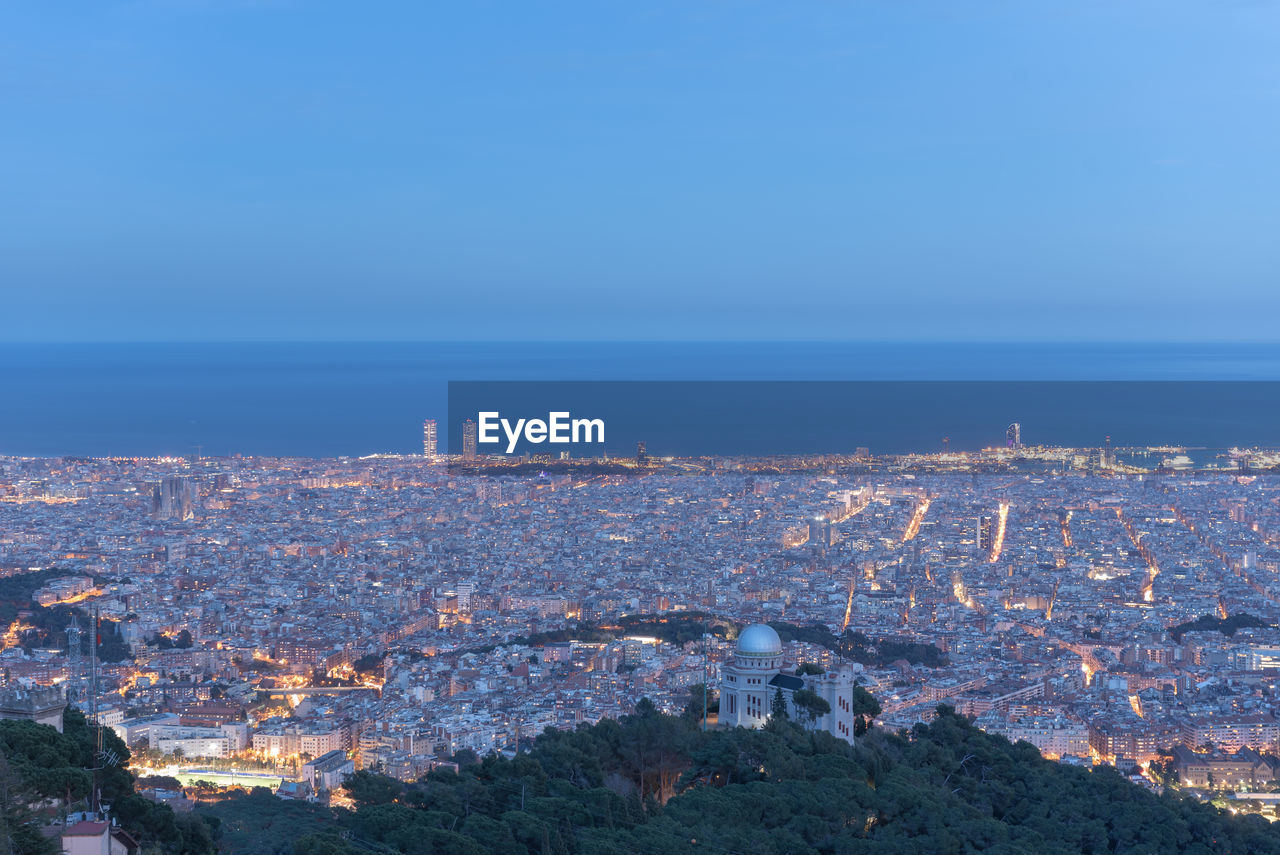 HIGH ANGLE VIEW OF ILLUMINATED BUILDINGS IN CITY AGAINST SKY