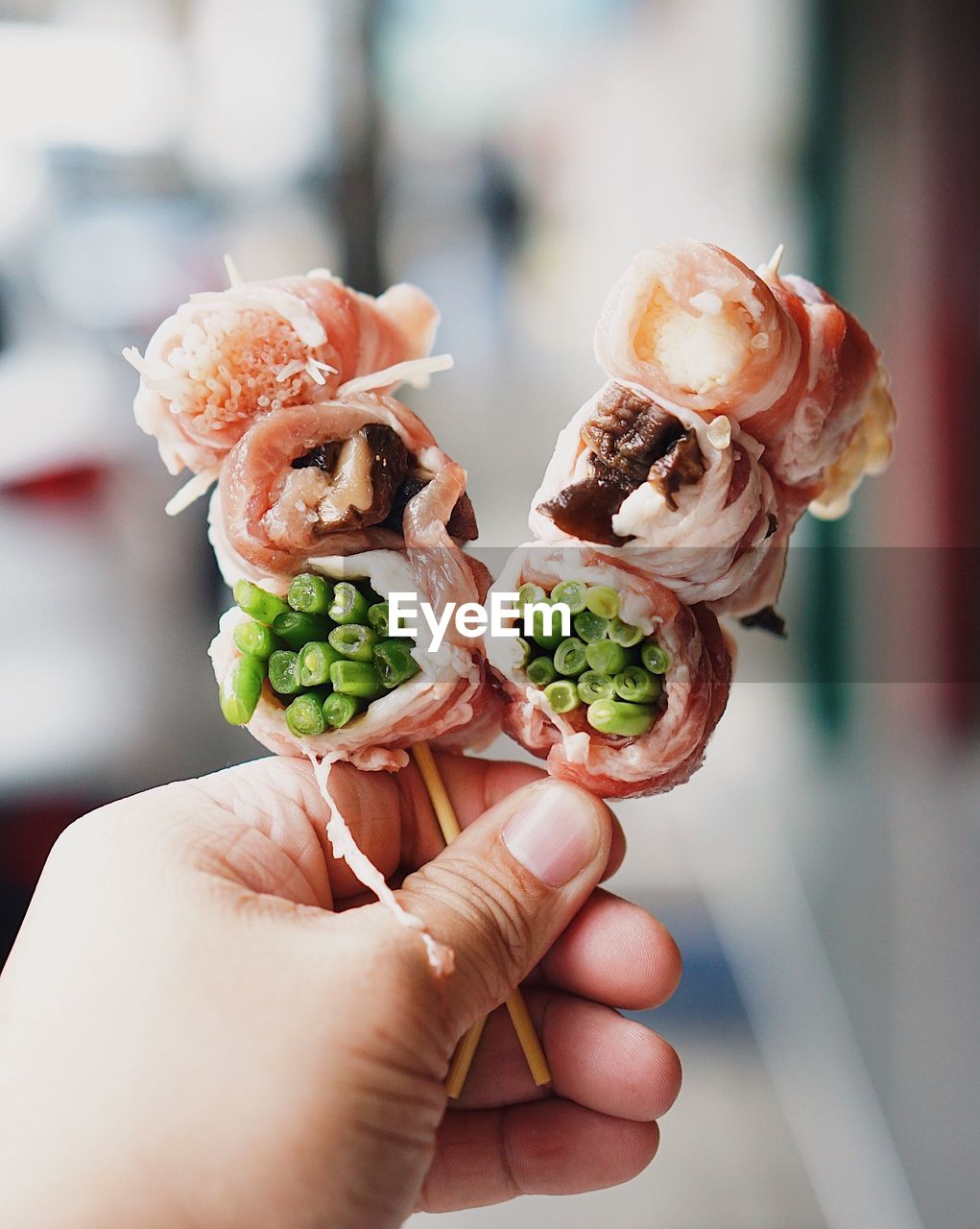 Cropped hand of man holding skewer meat rolls