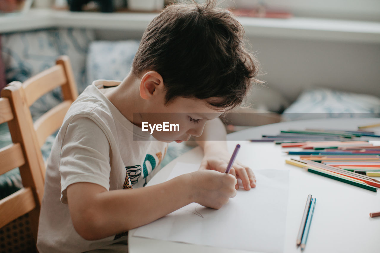 The boy draws with pencils at the kitchen, closeup. high quality photo