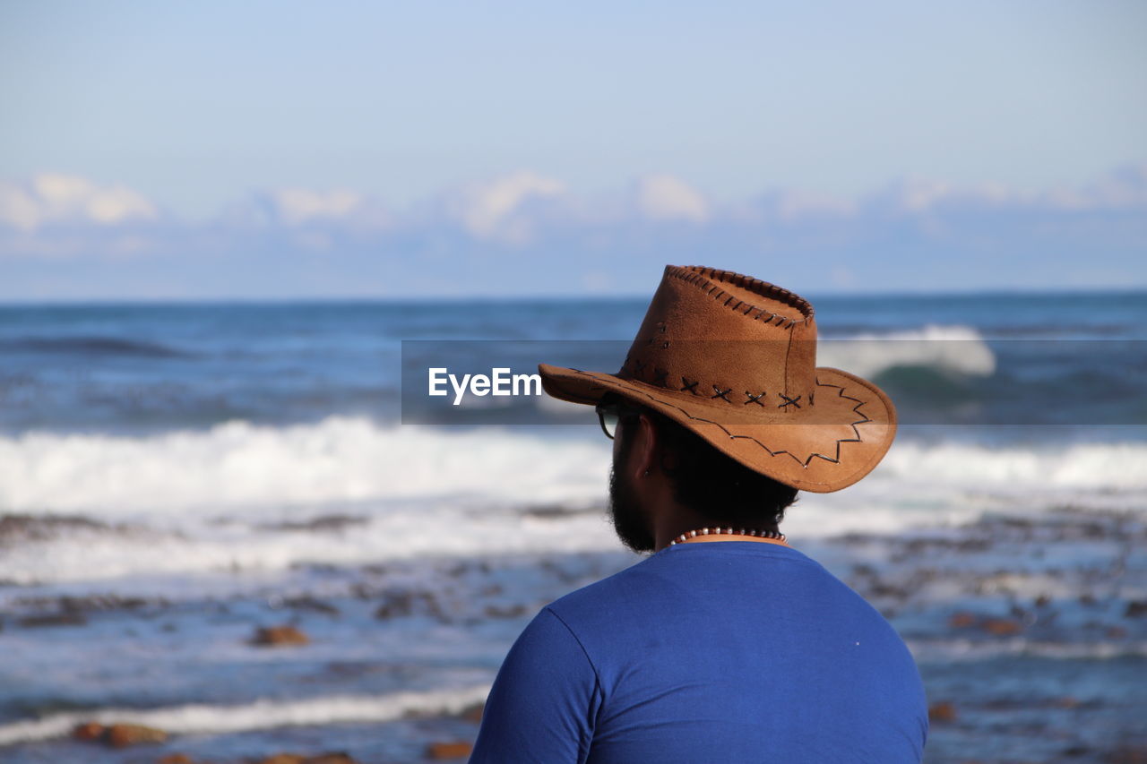 Rear view of man wearing hat sitting by sea