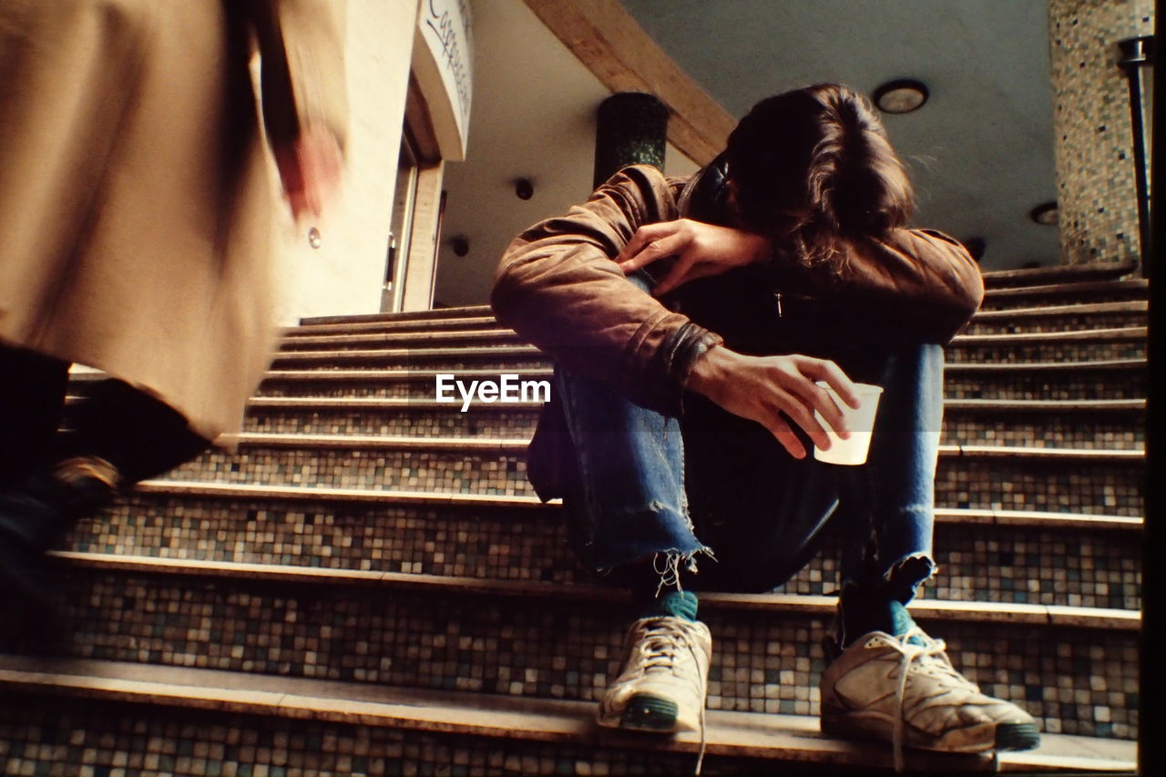 Sad man holding disposable cup sitting on steps