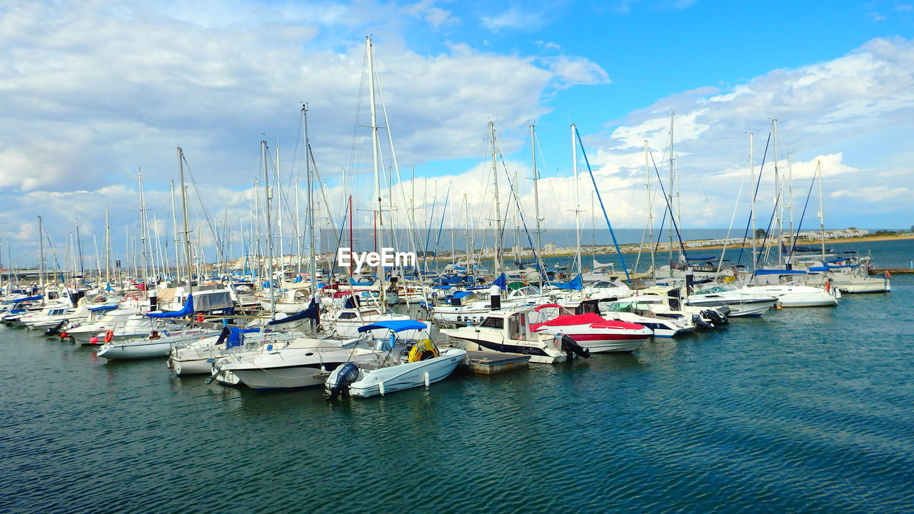 Sailboats moored on harbor against sky