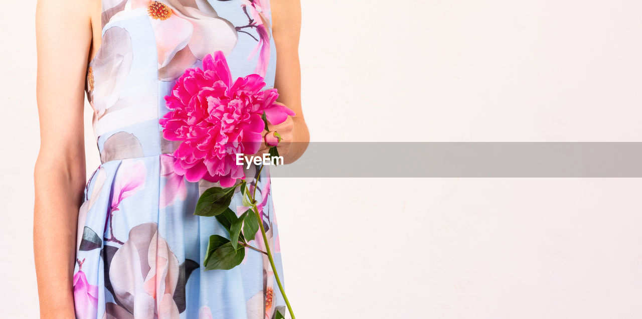 WOMAN HOLDING PINK FLOWER AGAINST WALL