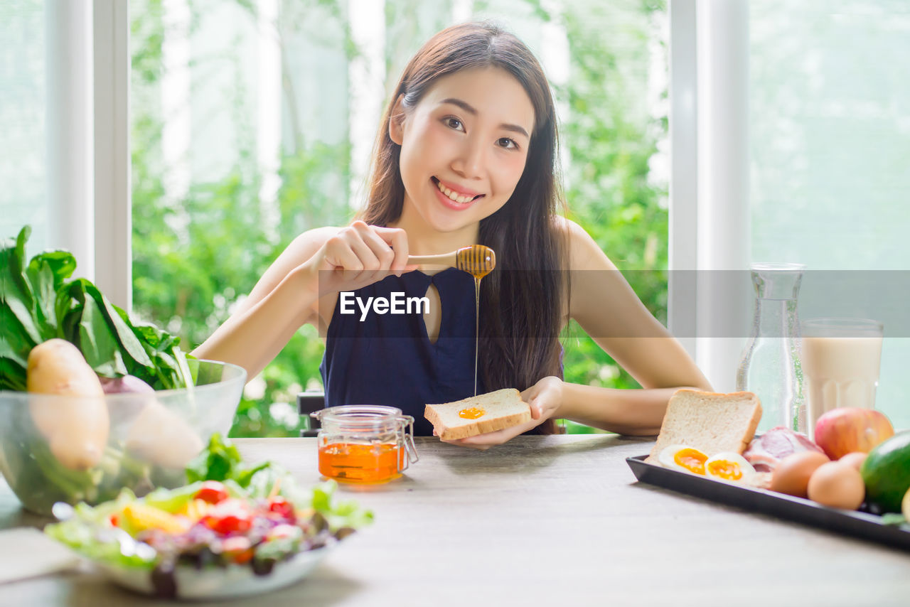 Portrait of young woman putting honey on bread