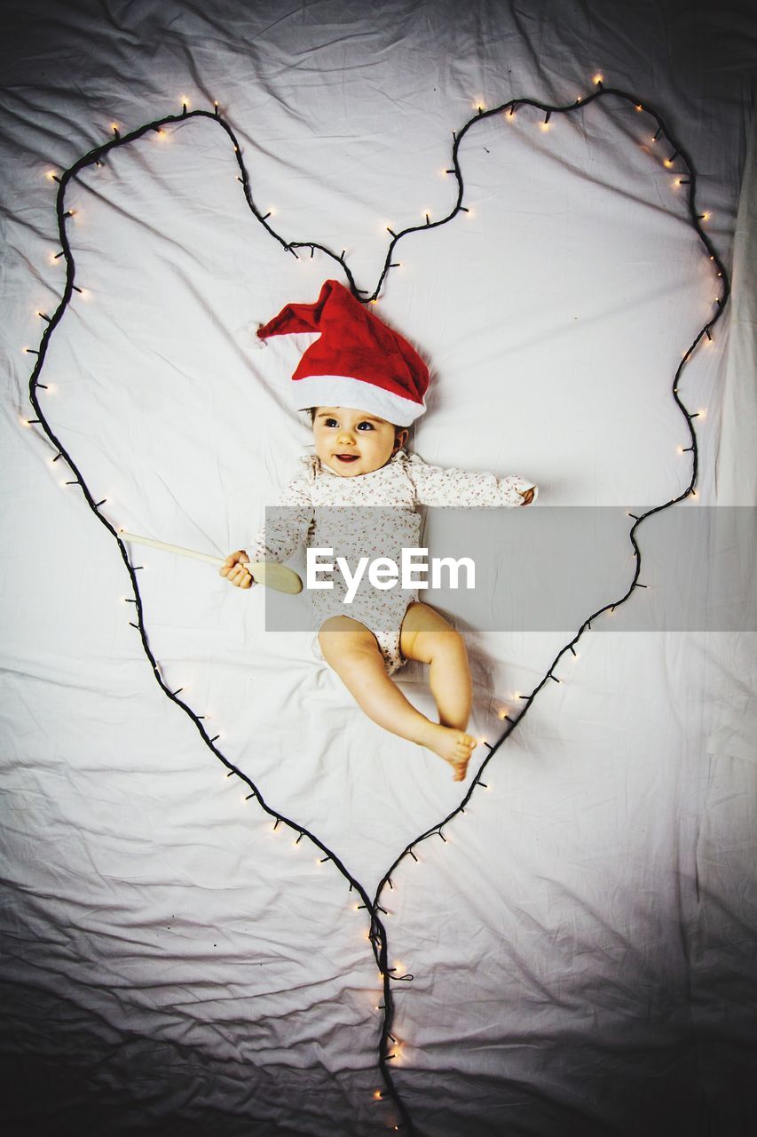 High angle view of baby lying on bed by illuminated heart shape lighting equipment