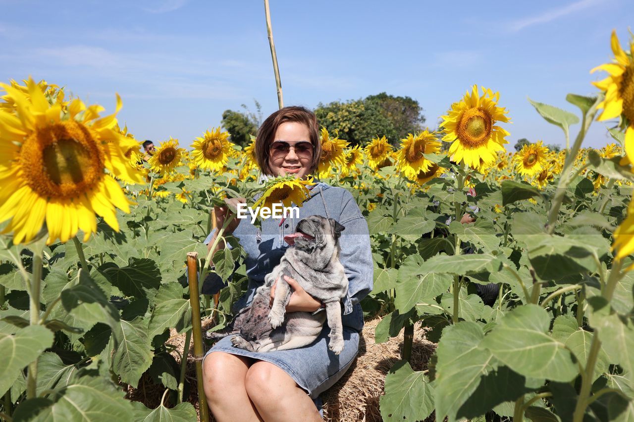 PORTRAIT OF SMILING WOMAN HOLDING SUNFLOWER AGAINST YELLOW WALL