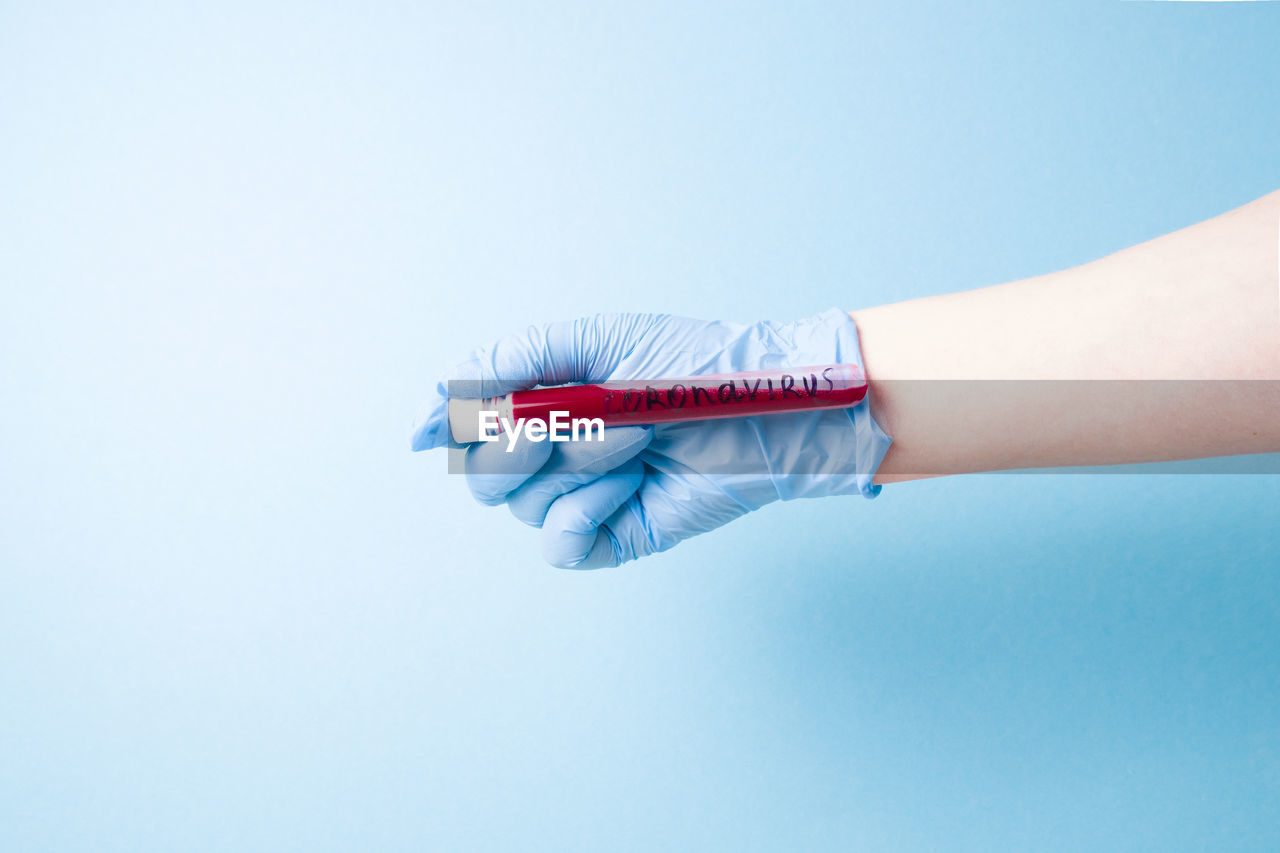 Close-up of woman hand holding test tube against blue background