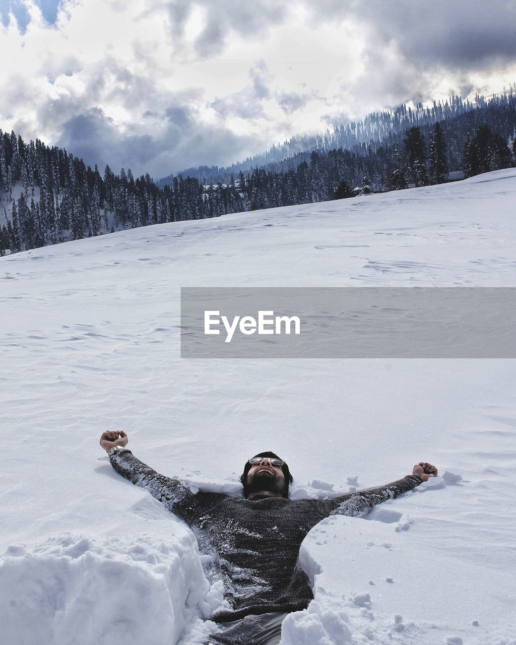 Man with arms outstretched lying on snow covered land