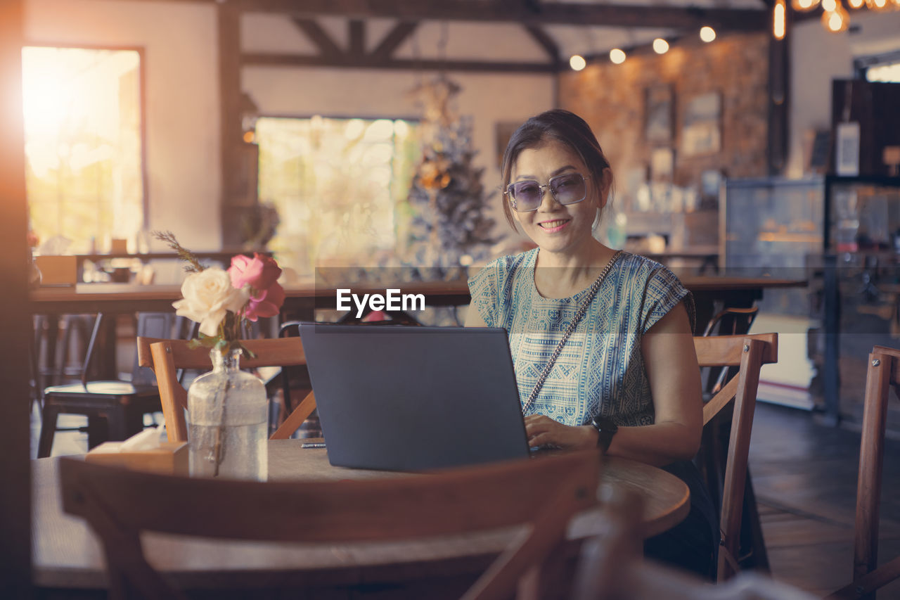 Portrait of smiling woman using laptop while sitting at cafe