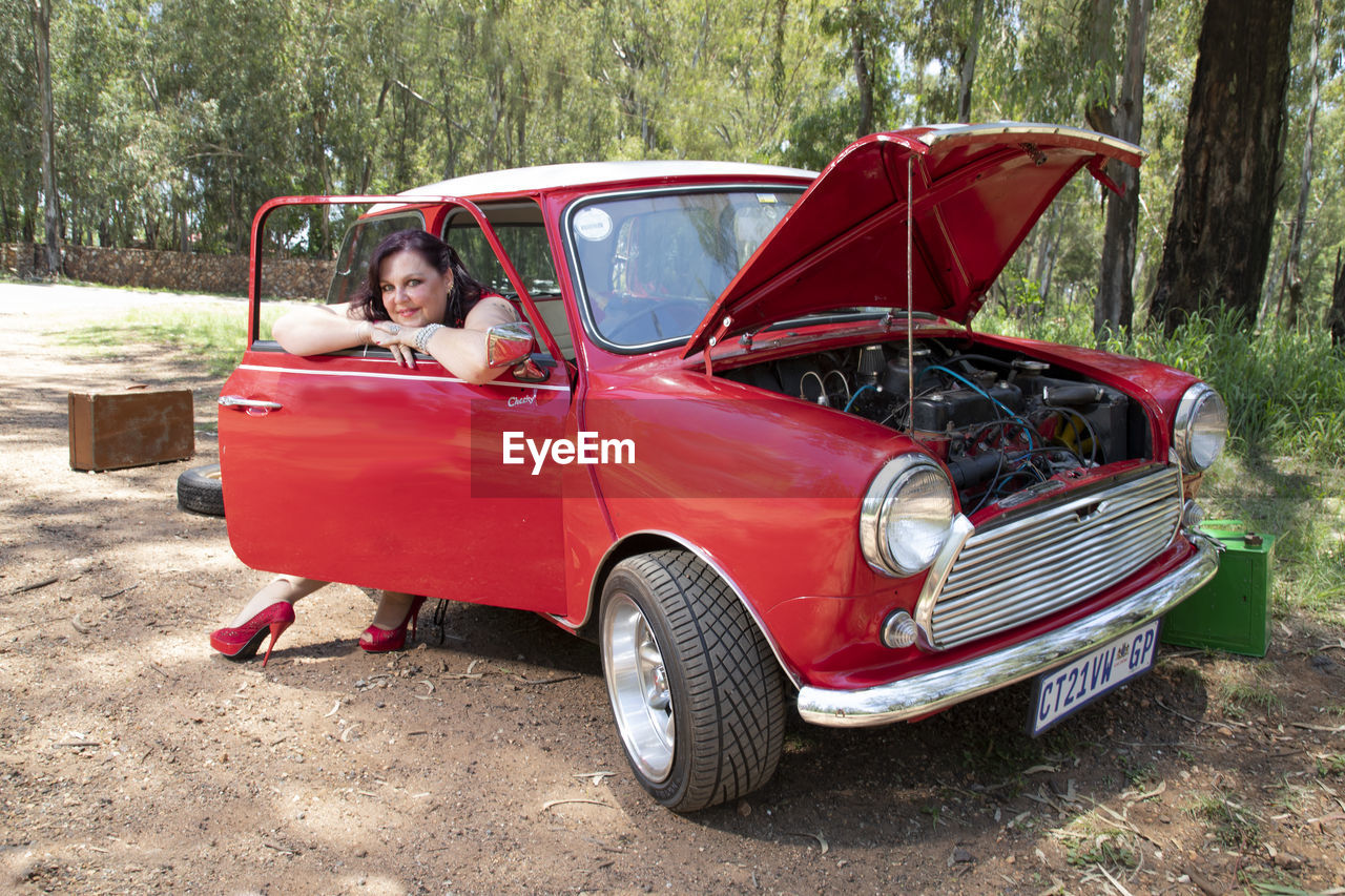 PORTRAIT OF WOMAN SITTING ON RED CAR