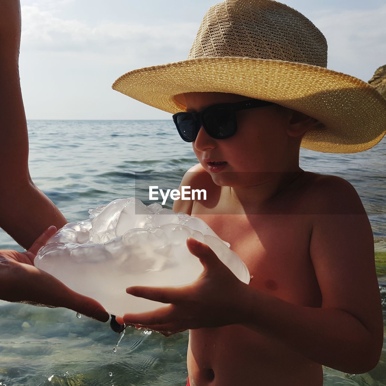 Cropped hands of person giving ice to boy standing at beach